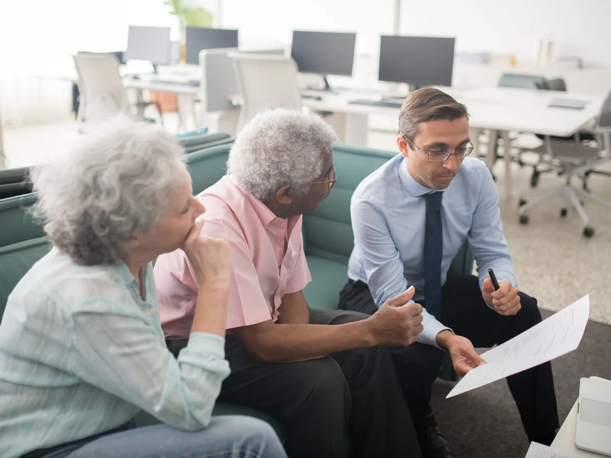 An older couple discuss a document with a man seated beside them.