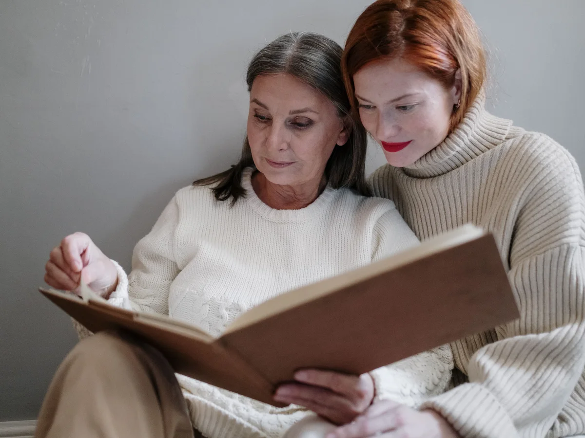 Two women look through a book together at home.