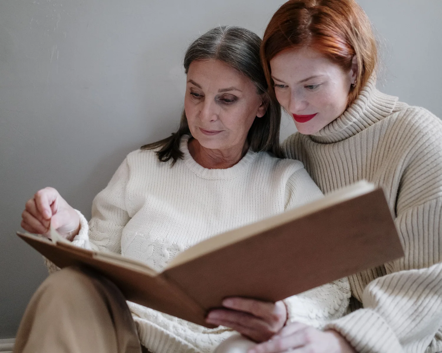 Two women look through a book together at home.