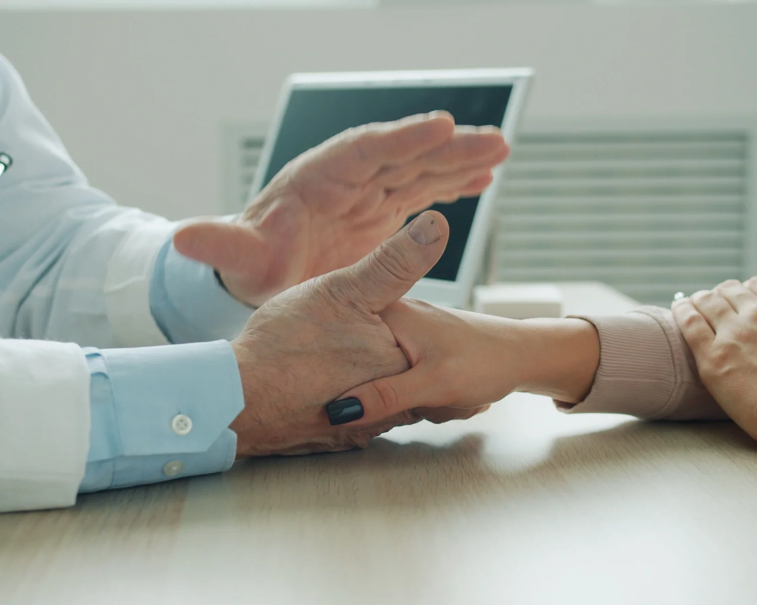 A clinician examines a person's hand and wrist across a desk.