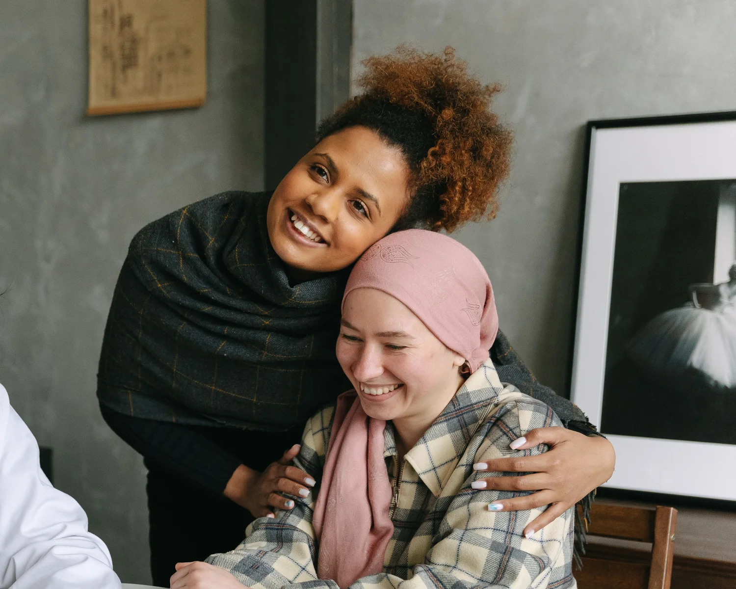 A woman in a head wrap smiles as a friend hugs her.