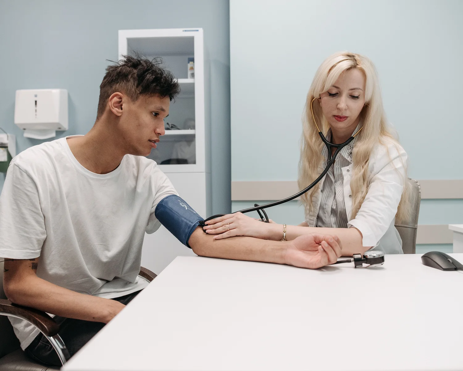 A clinician checks a seated man's blood pressure with a manual cuff.