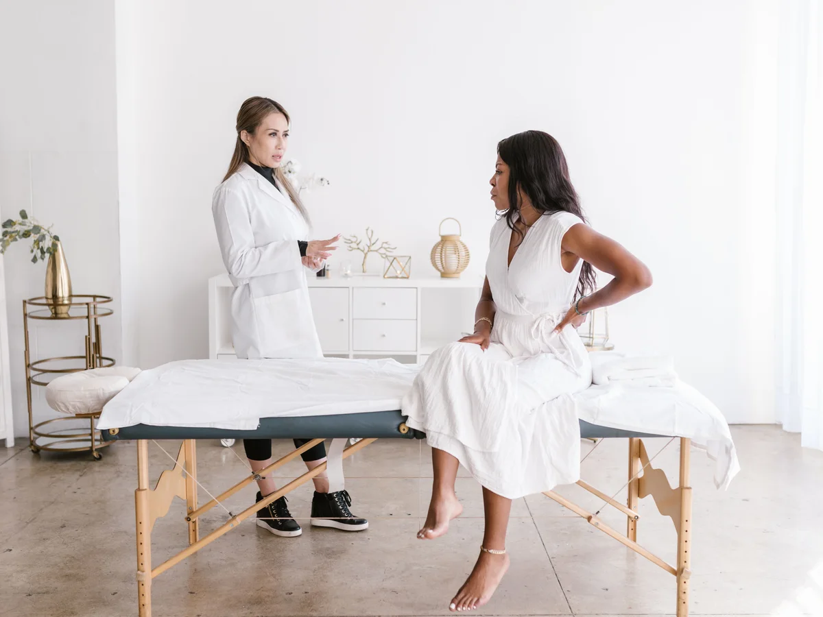 A woman discusses her back with a clinician in a bright treatment room.