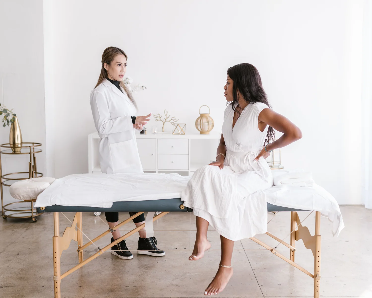 A woman discusses her back with a clinician in a bright treatment room.