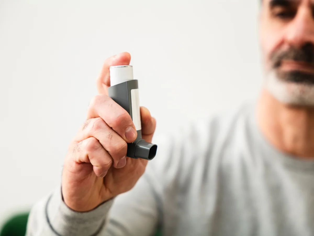 A man holds an unbranded inhaler in his hand.