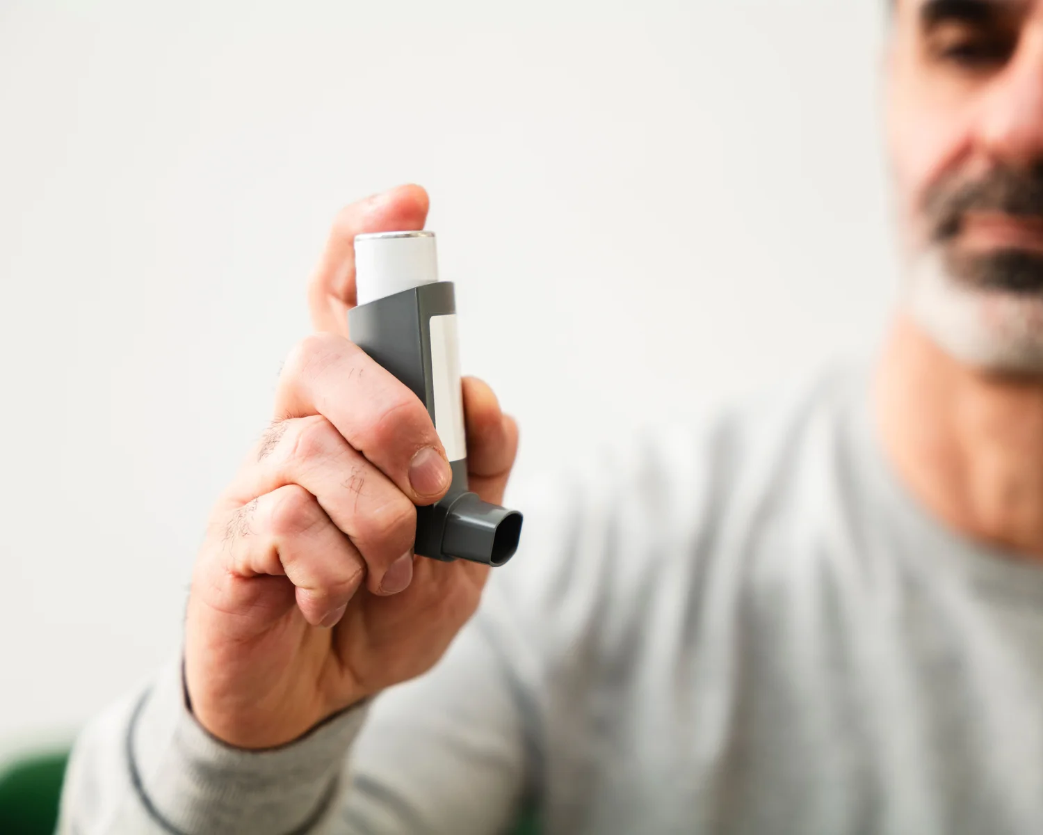 A man holds an unbranded inhaler in his hand.