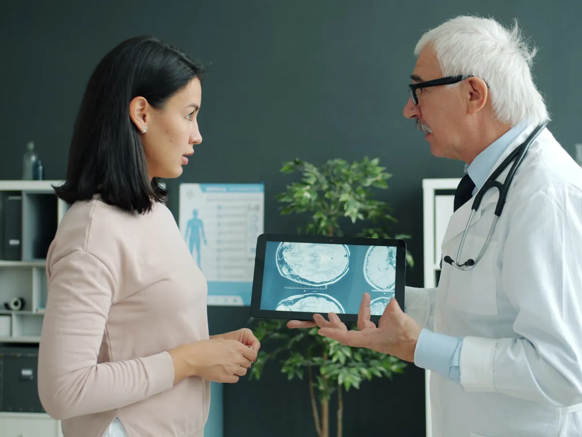 A doctor shows a woman brain scans on a tablet and talks her through them.