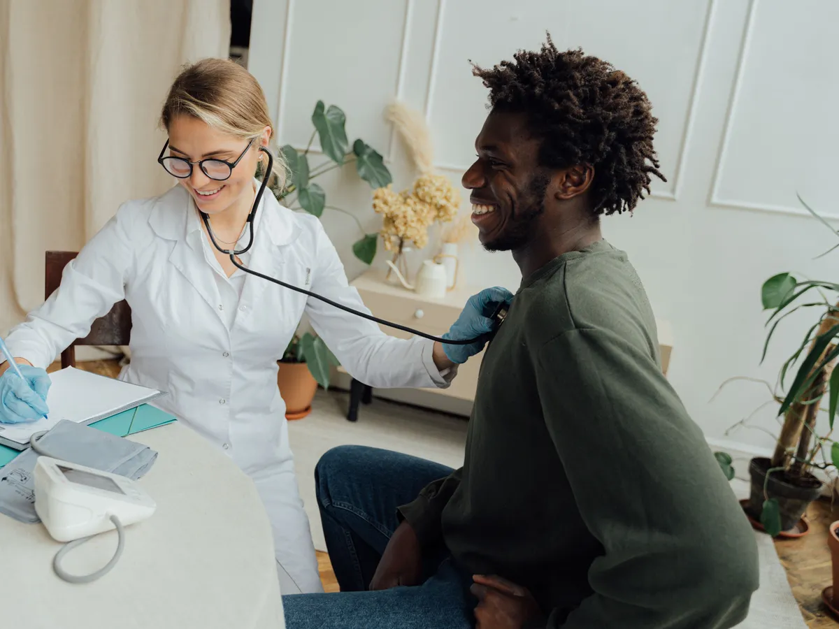A smiling doctor listens to a man's heart with a stethoscope during a check-up.