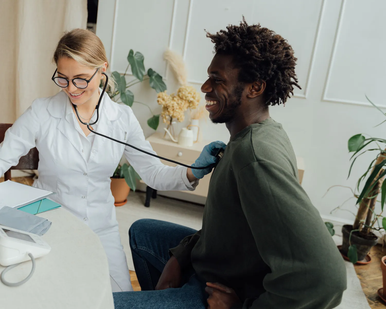 A smiling doctor listens to a man's heart with a stethoscope during a check-up.