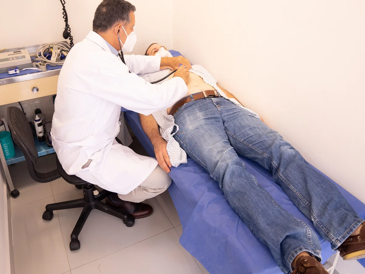 A clinician examines a man lying on an examination table.
