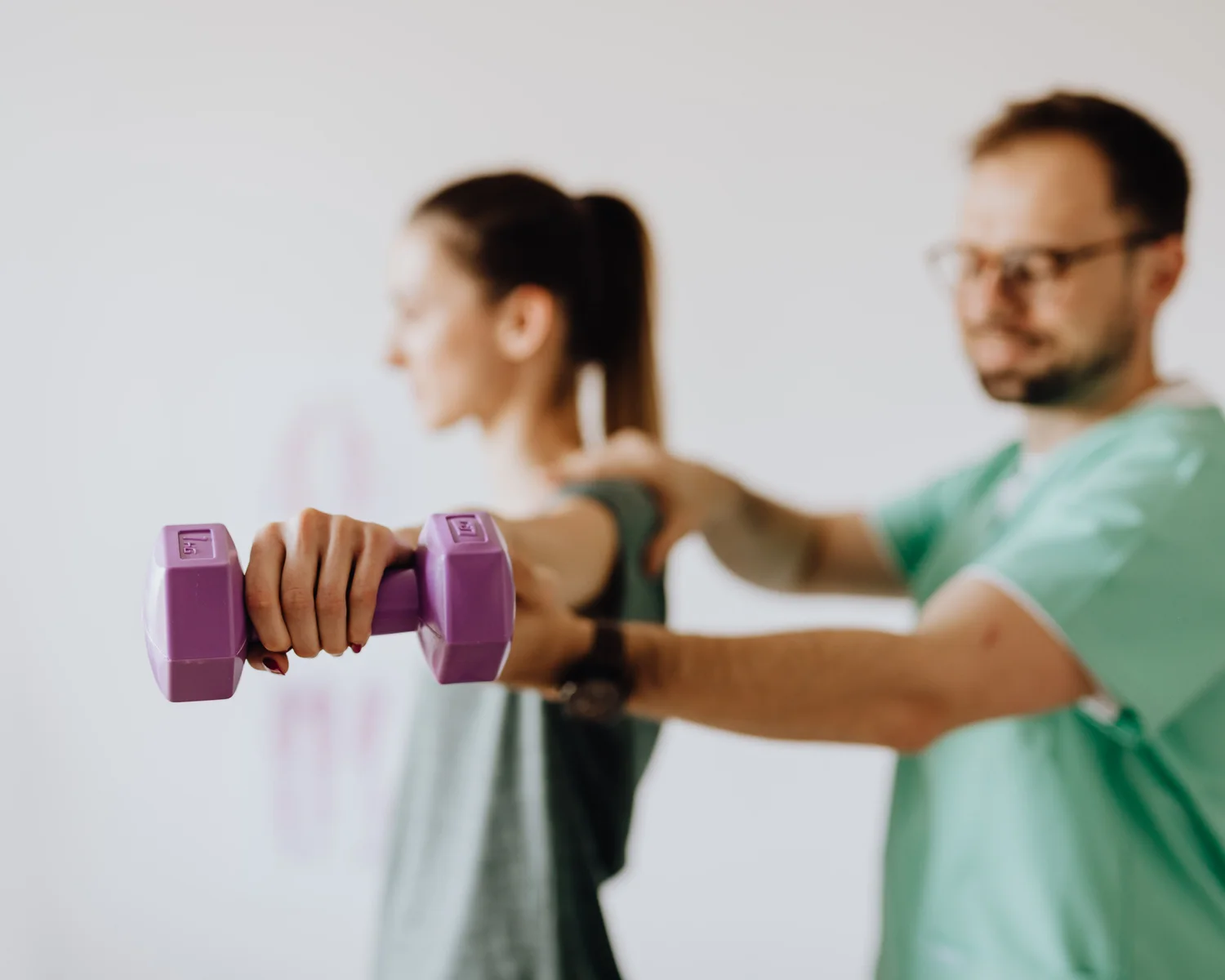 A therapist supports a woman during a shoulder exercise with a small weight.