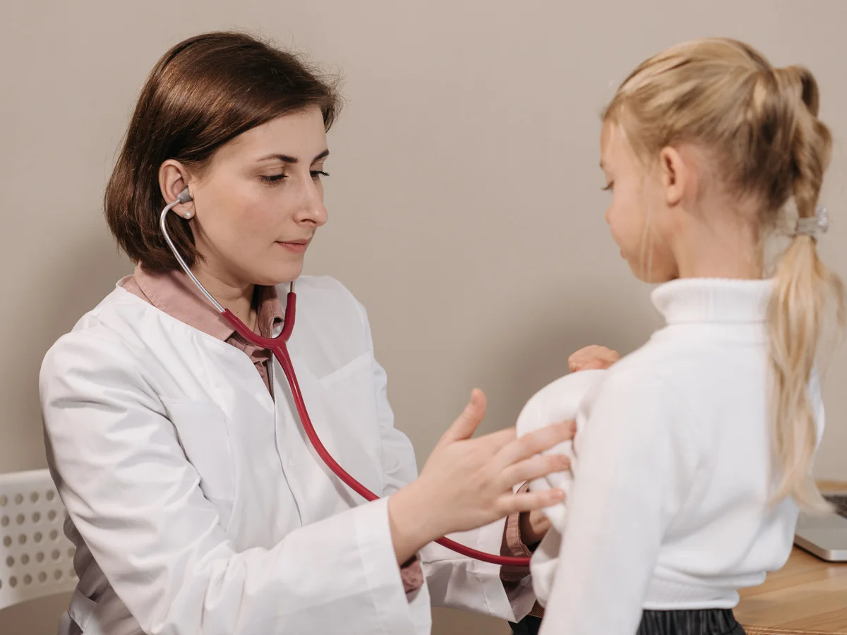 A clinician uses a stethoscope to examine a child during a check-up.