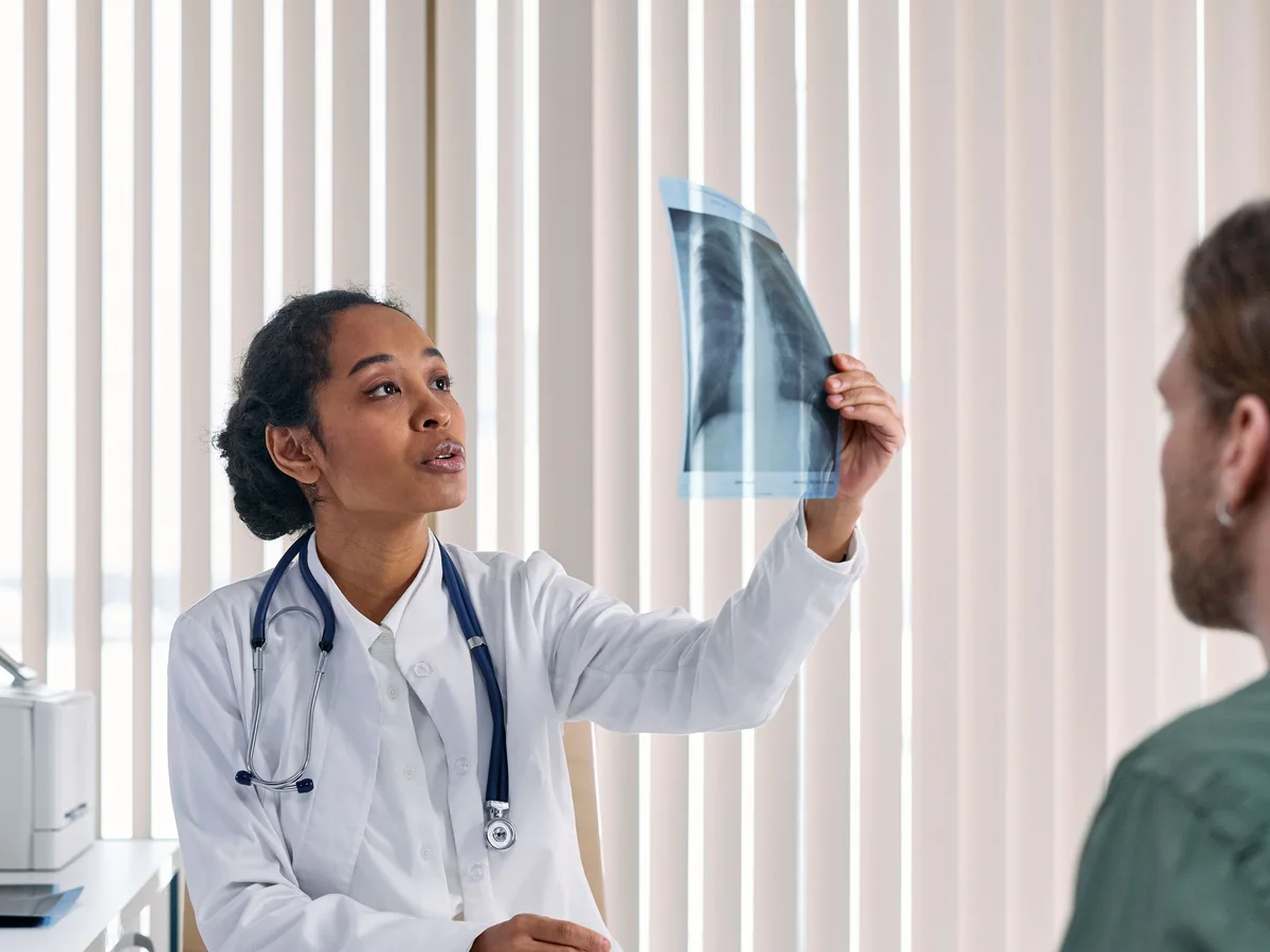 A clinician explains an X-ray to a seated man.