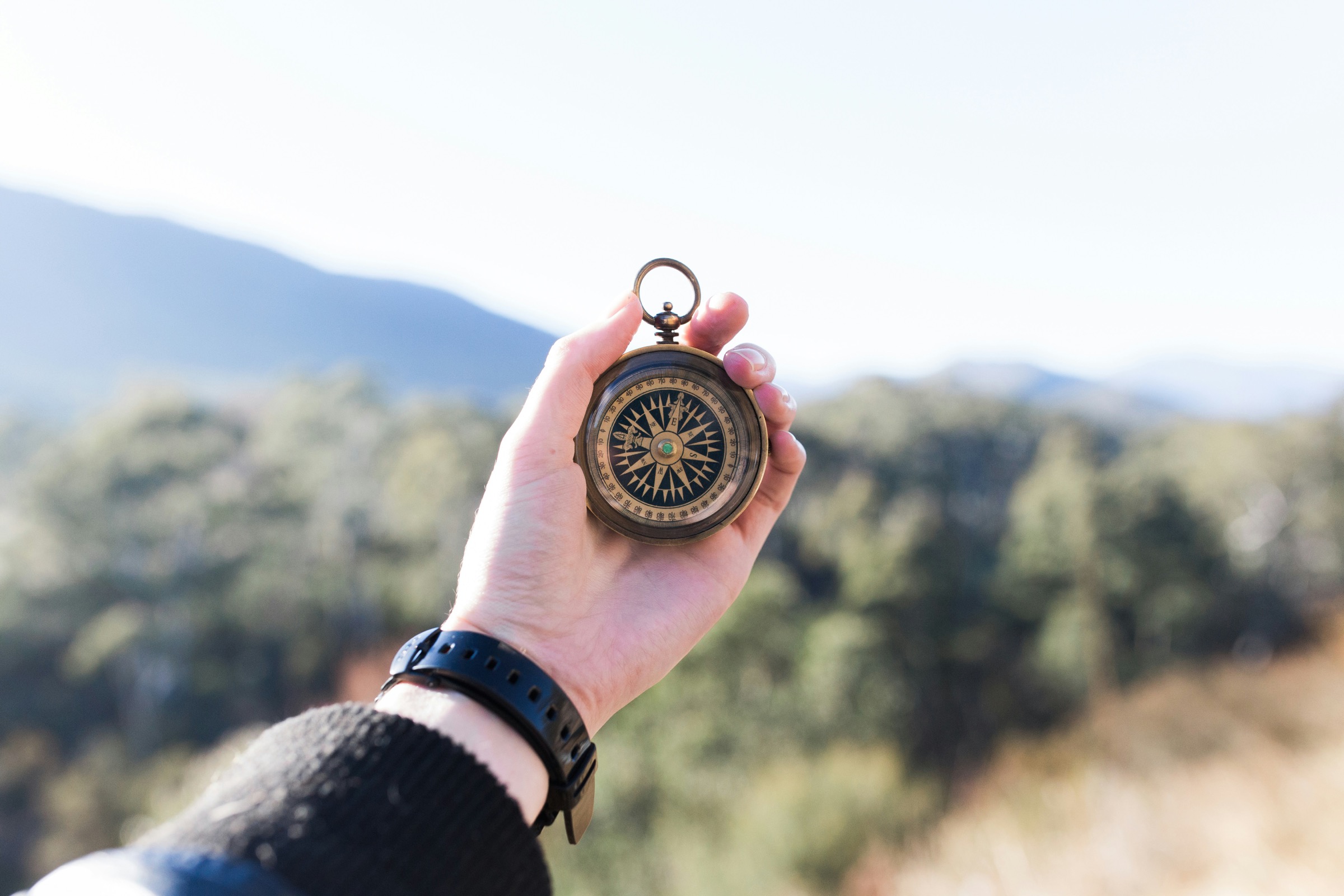 A hand holding an open brass compass against a blurred mountain landscape