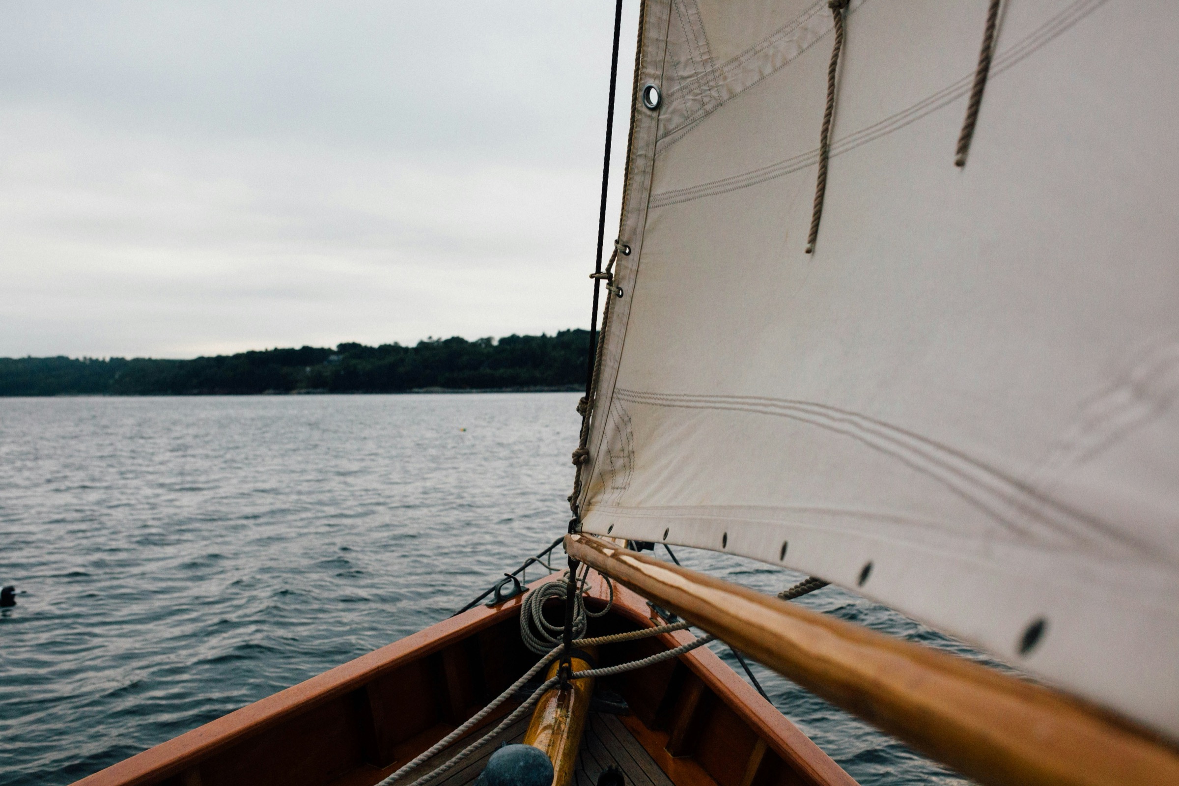 View from inside a small wooden sailboat with its sail up on open water