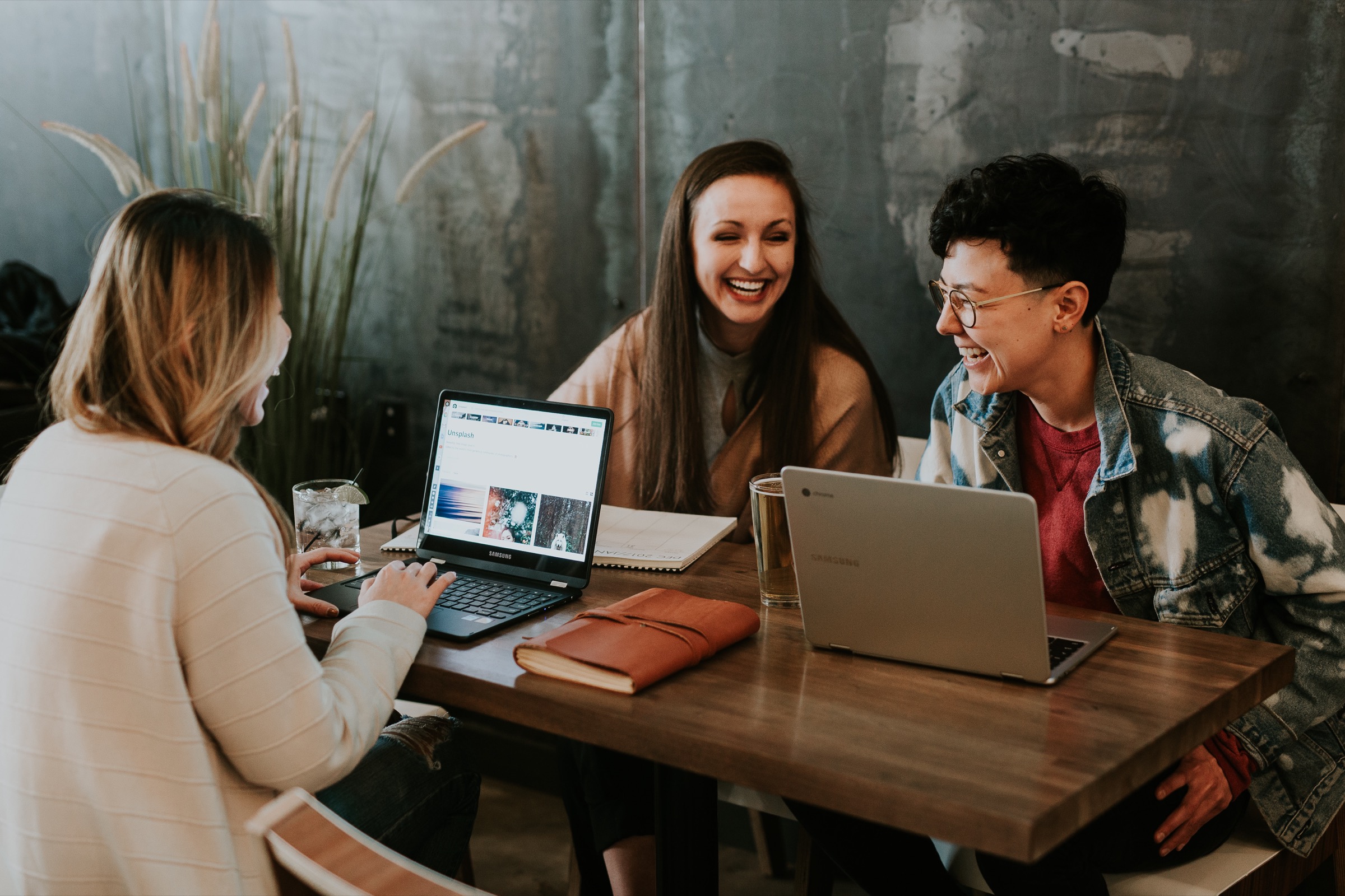 Three young women laughing together around a table with laptops