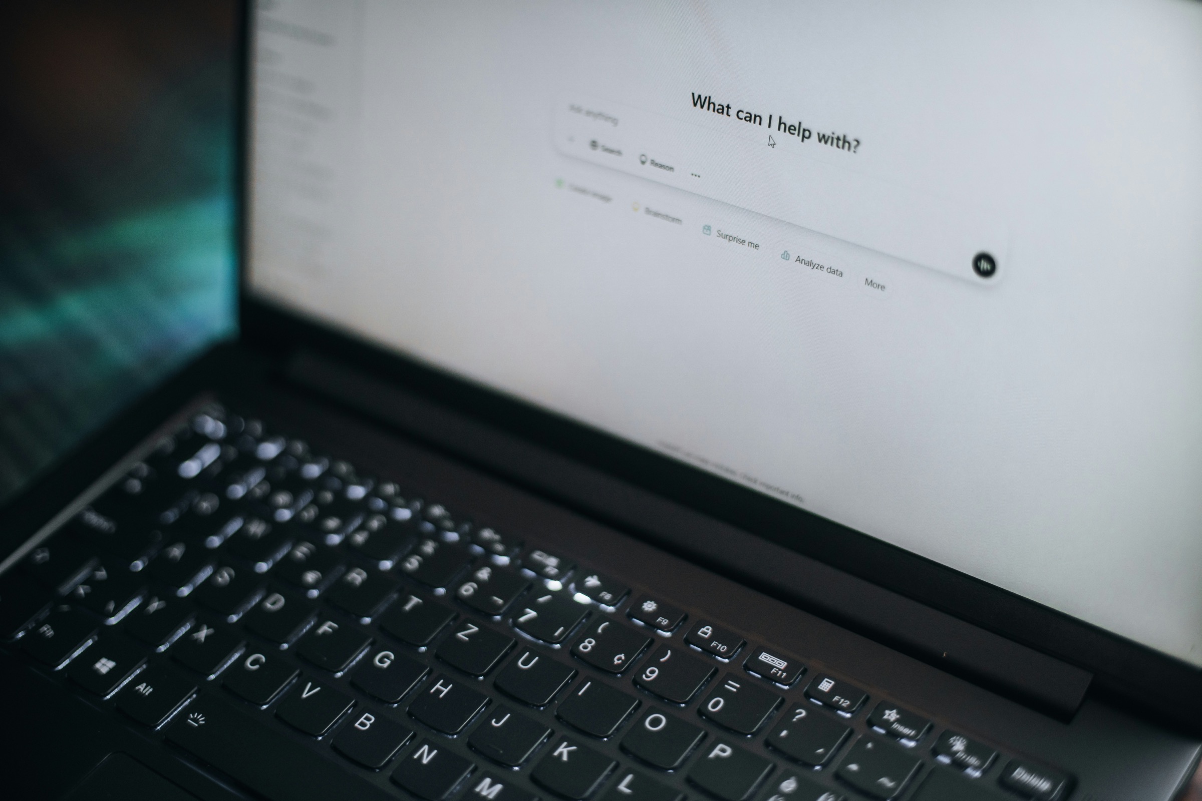 Close-up of a laptop screen showing a chat assistant asking "What can I help with?"