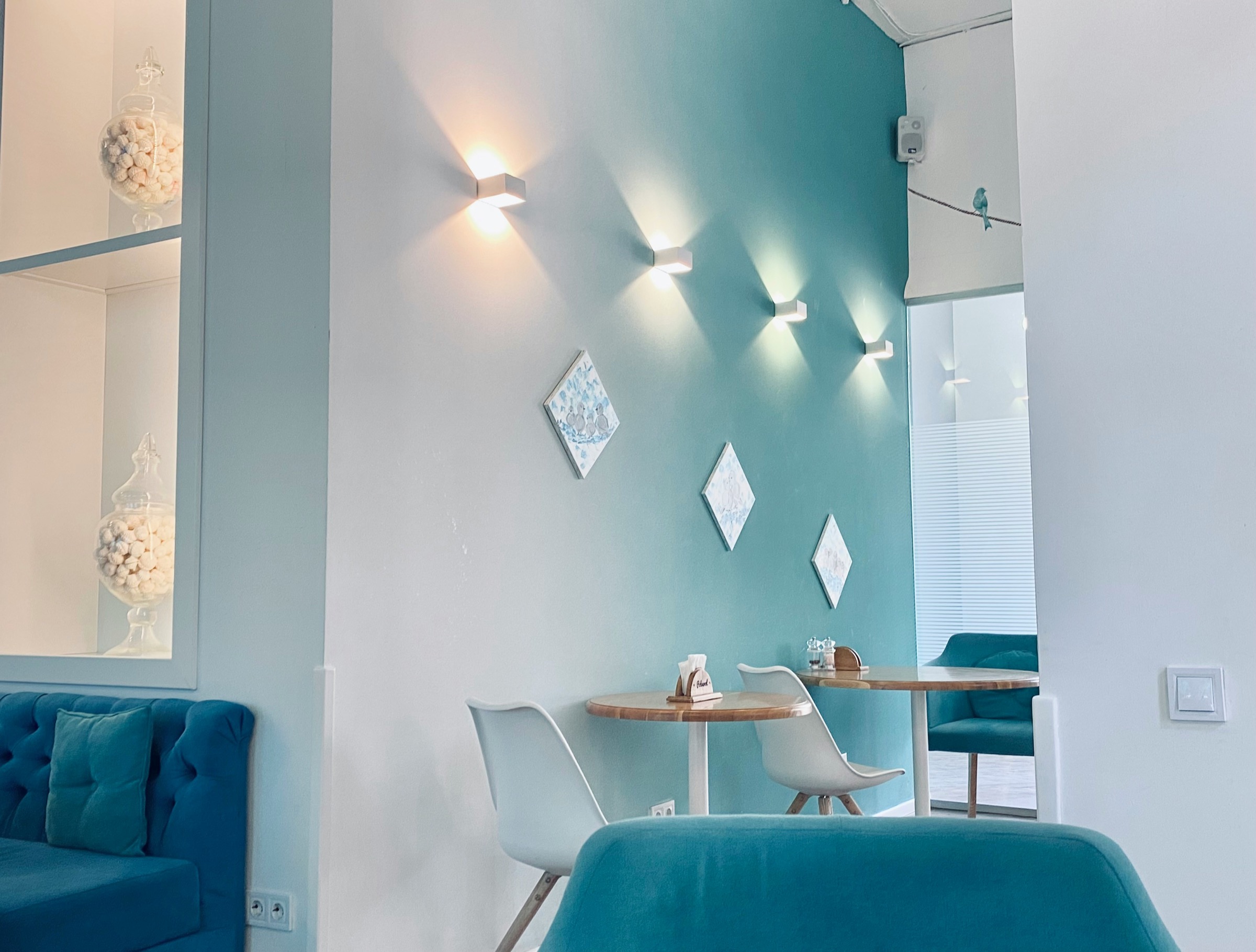 A bright, modern waiting area with teal walls, wall lights and blue armchairs