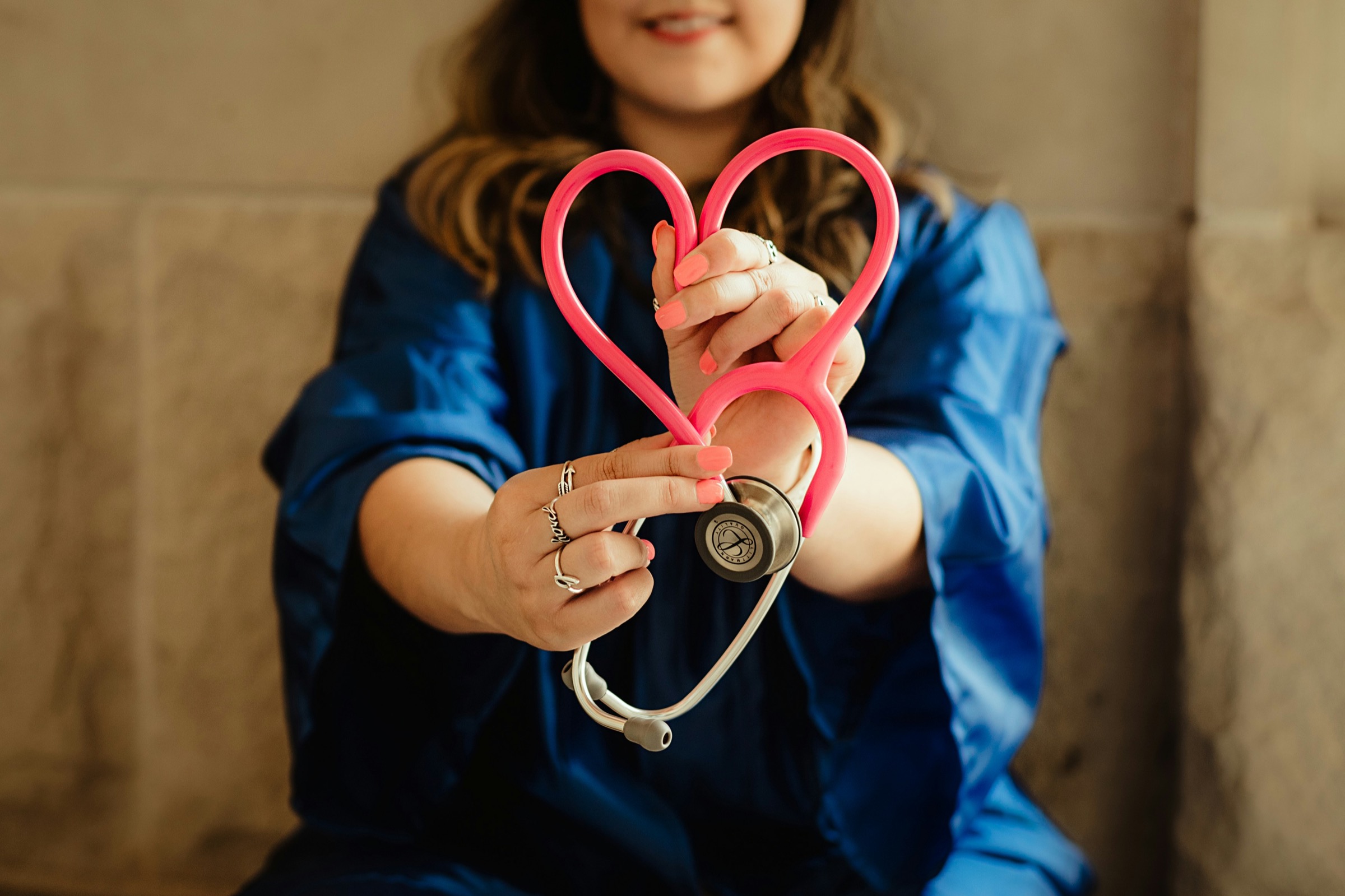 A person in blue scrubs holding a stethoscope shaped into a heart
