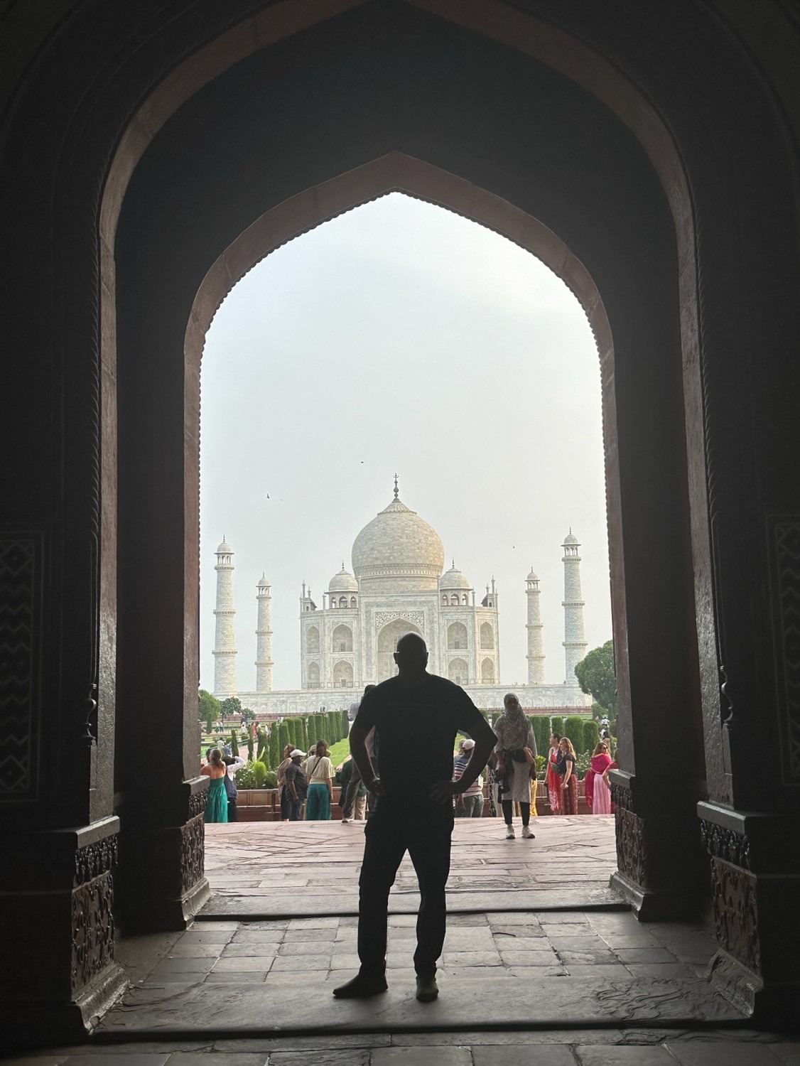 A man silhouetted in a dark archway, looking out toward the Taj Mahal