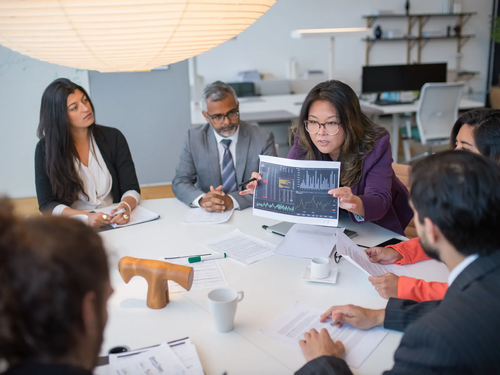 A group of colleagues meets around a table as one of them presents a chart.